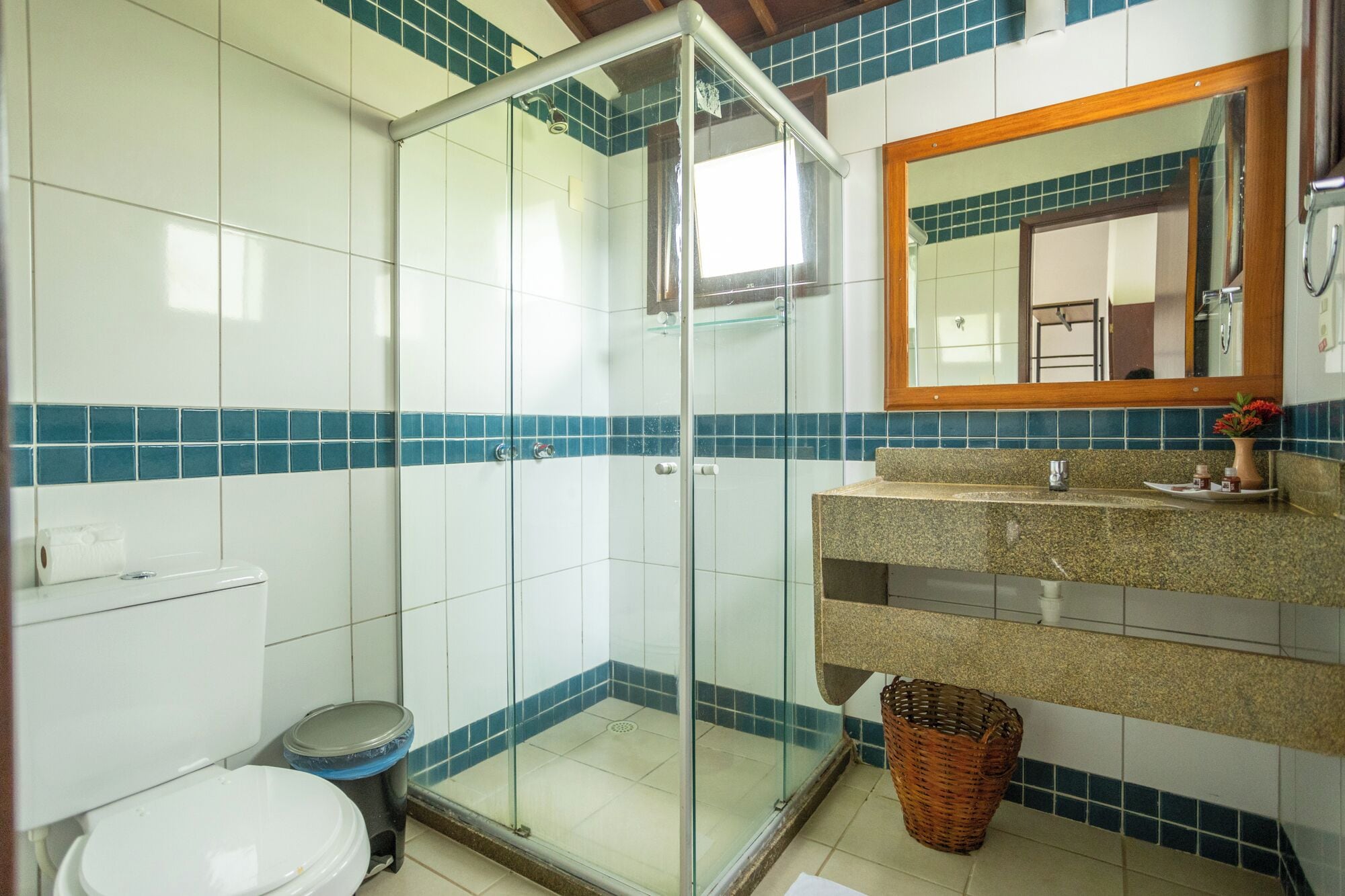 A bathroom with a glass shower enclosure, a toilet, a sink with a mirror, and a basket.