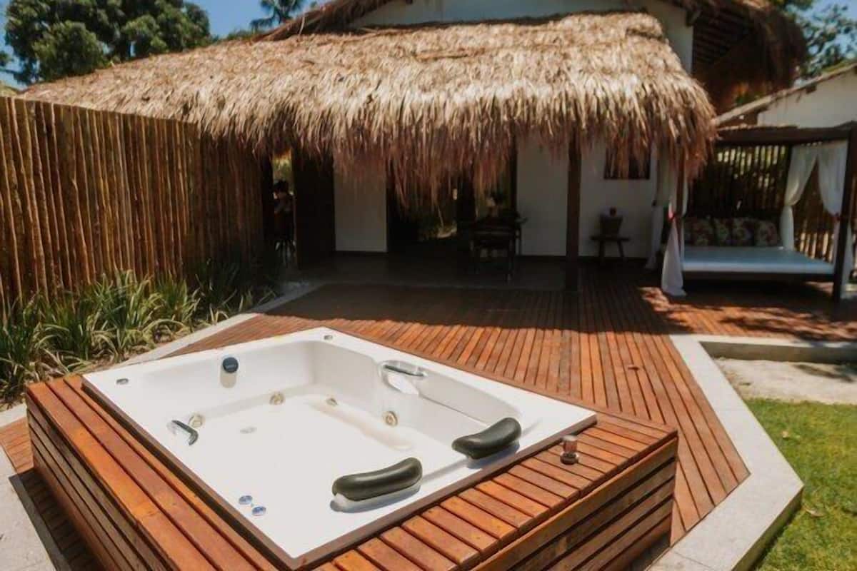 Un bain à remous installé sur une terrasse en bois, avec une structure à toit de chaume en arrière-plan.