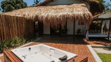 Un jacuzzi en un área de terraza de madera con una estructura de techo de paja al fondo.