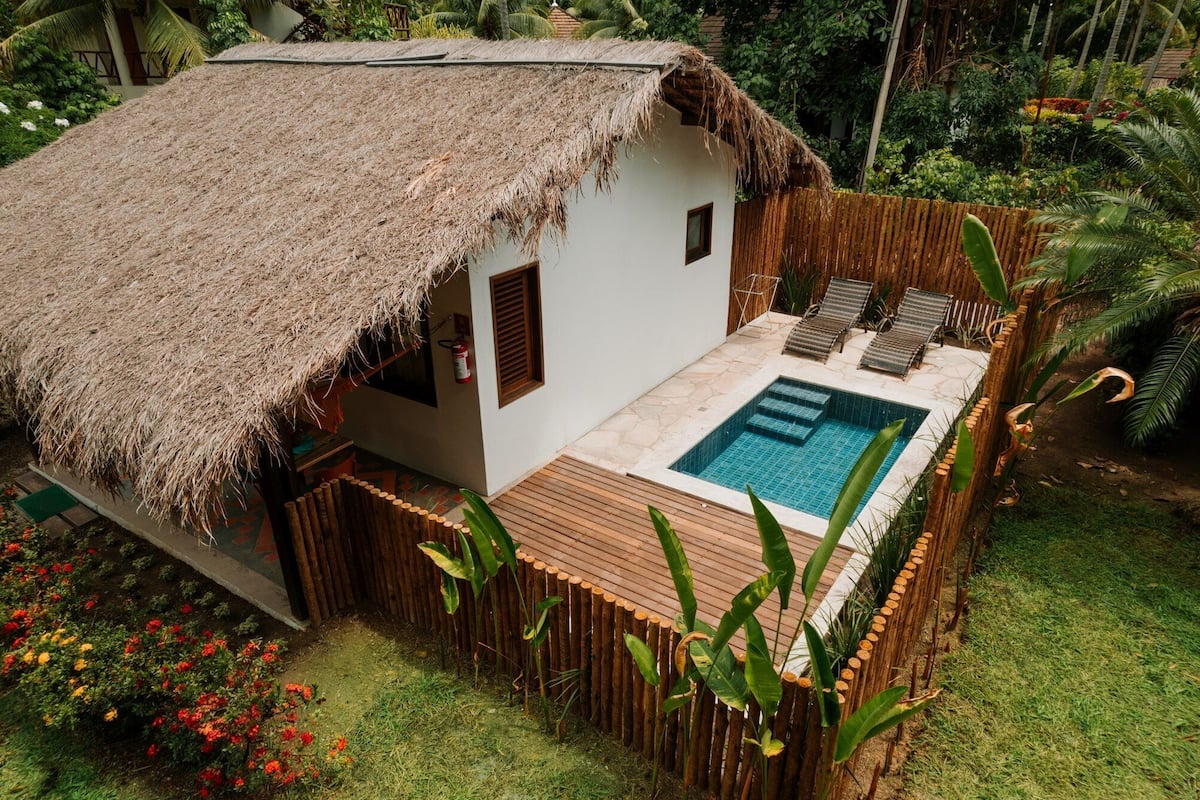 Une maison à toit de chaume avec une piscine et des chaises longues.