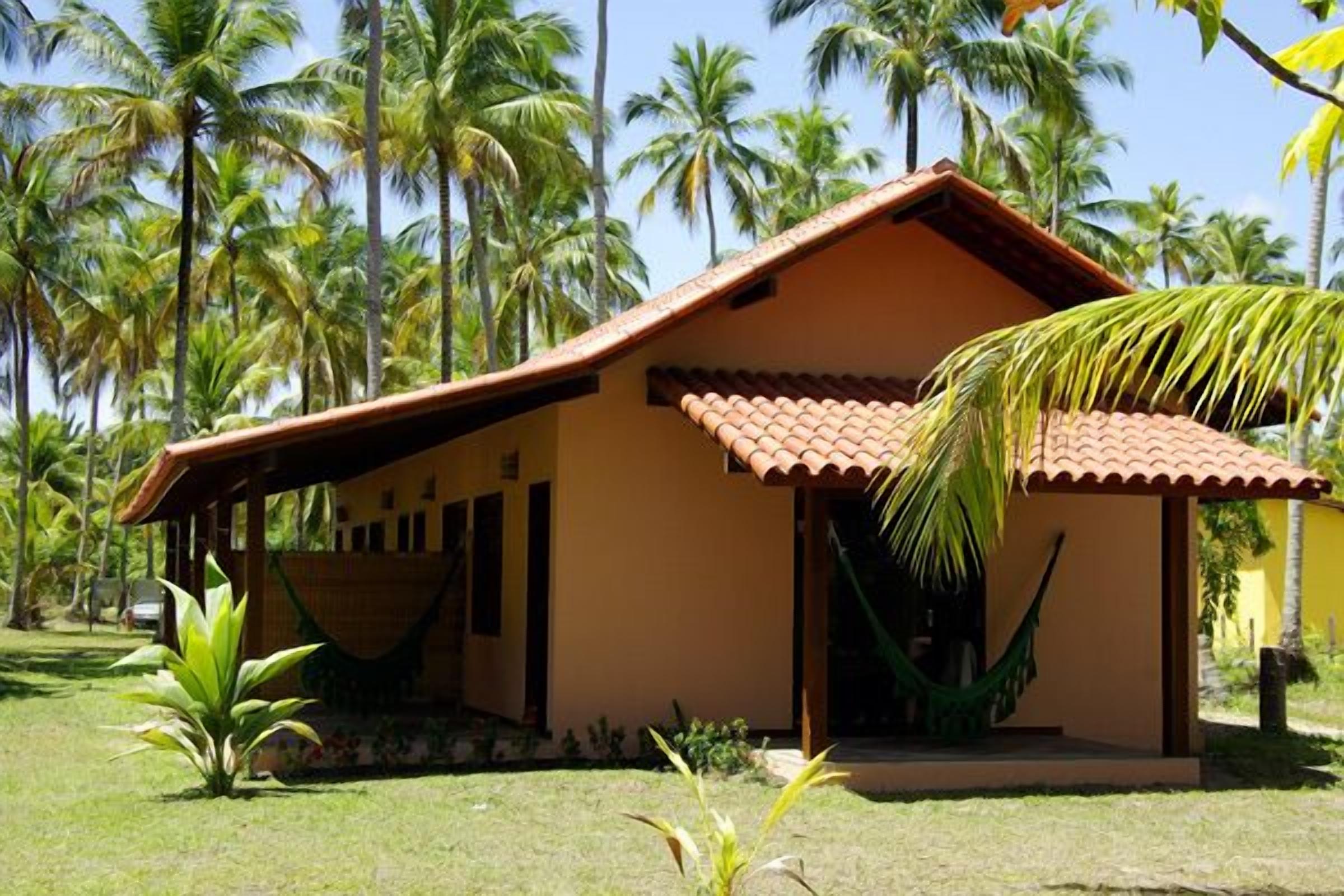 A small, single-story building with a tiled roof, surrounded by palm trees and a grassy area.