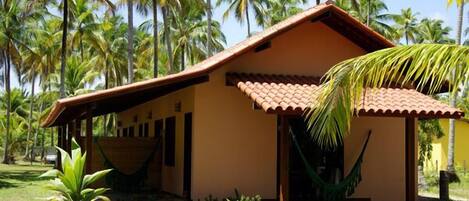 A small, single-story building with a tiled roof, surrounded by palm trees and a grassy area.