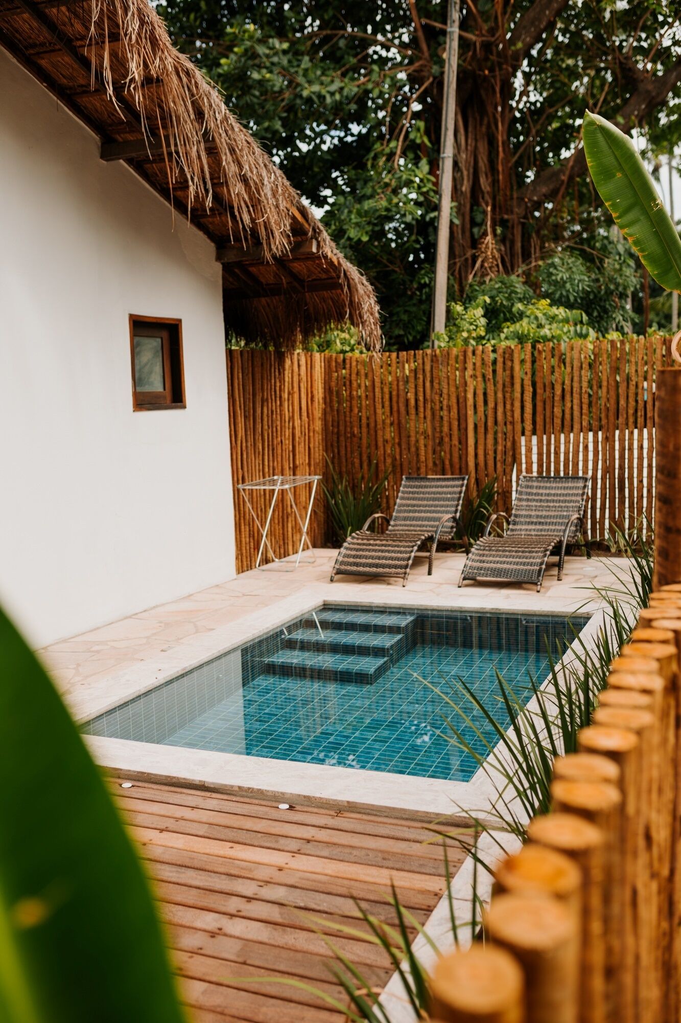 Une piscine dotée d’une terrasse en bois, de chaises longues et d’une structure surmontée d’un toit de chaume.