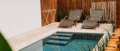 Une piscine dotée d’une terrasse en bois, de chaises longues et d’une structure surmontée d’un toit de chaume.