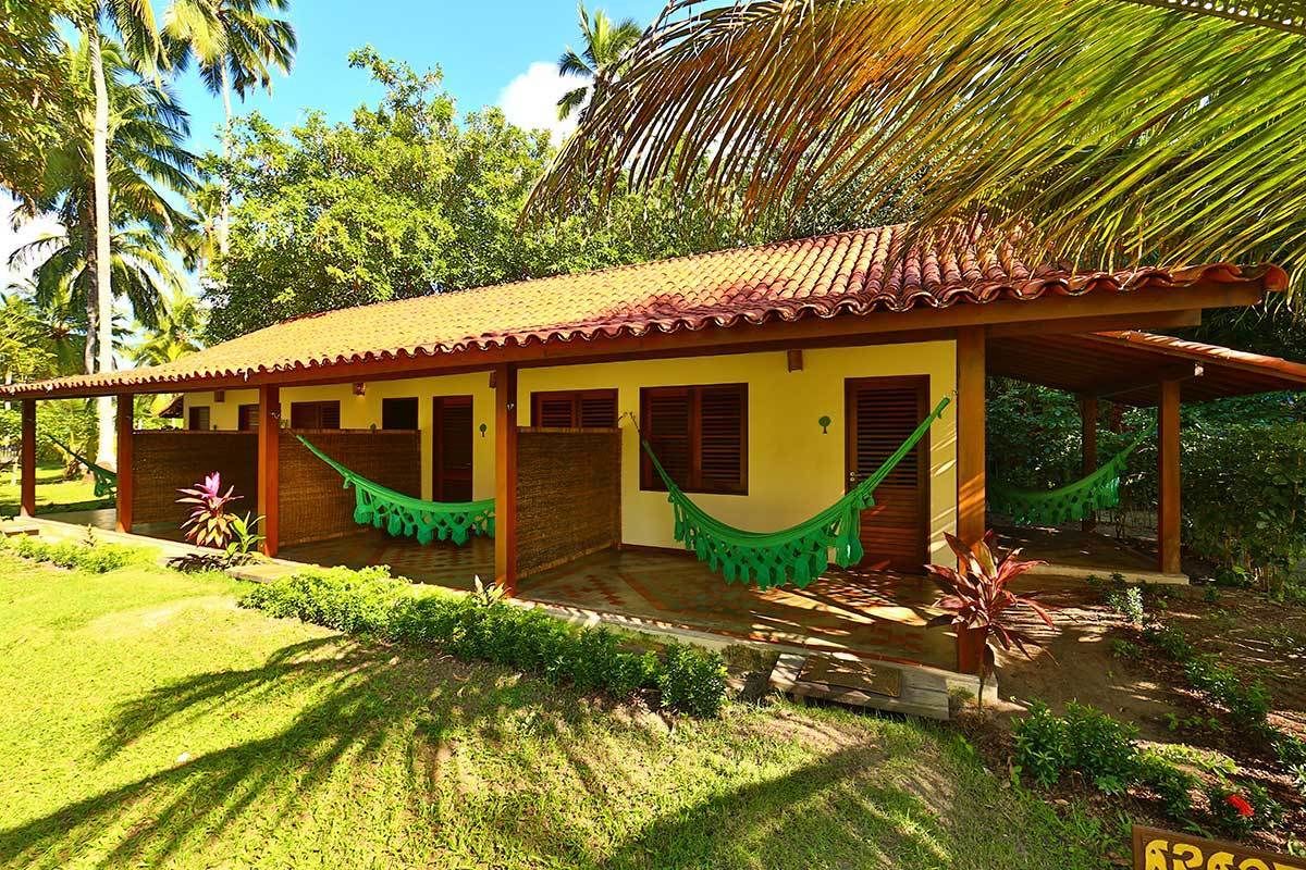 A house with a tiled roof, a porch with a hammock, and lush greenery around.