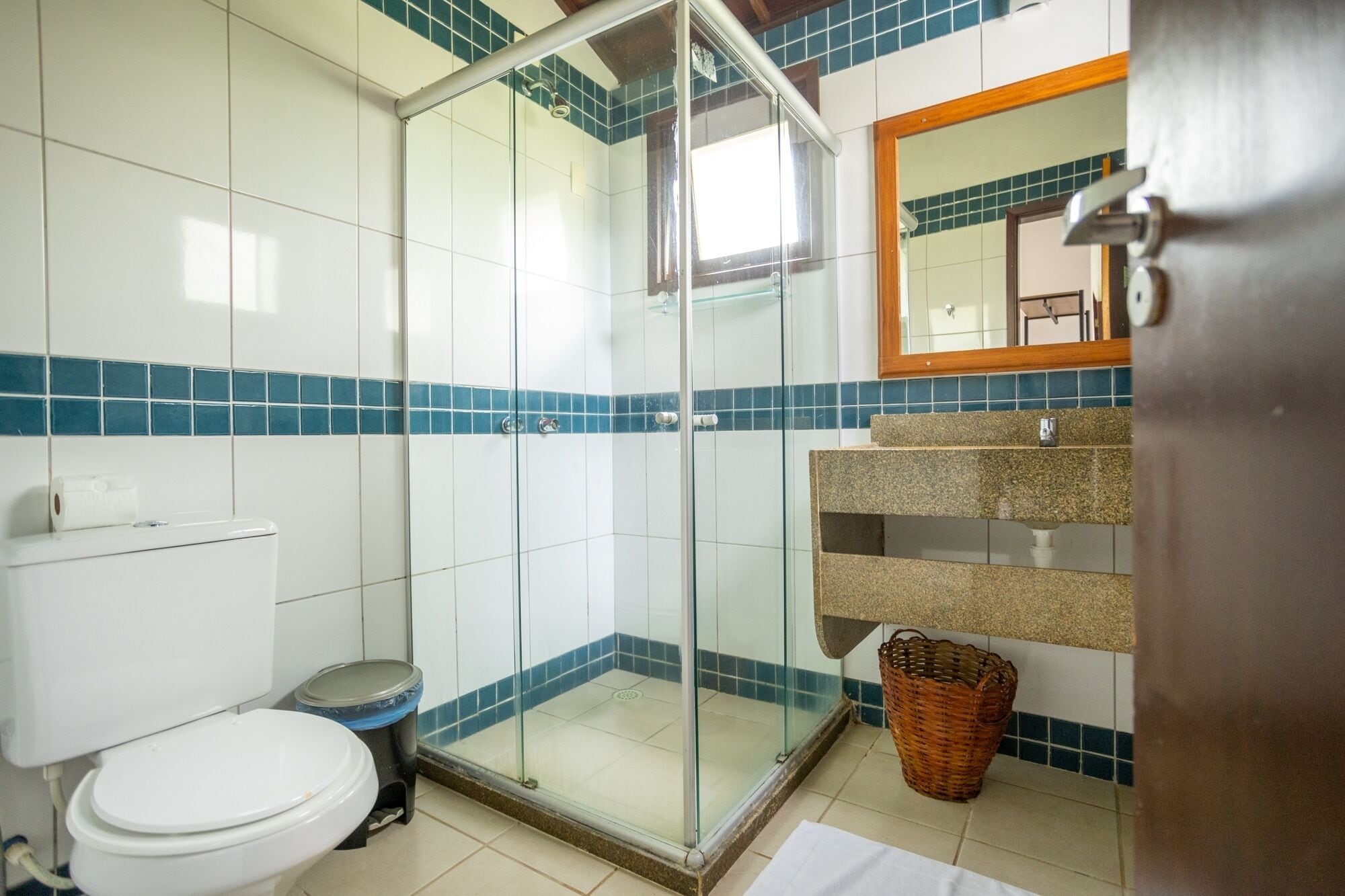 Et badeværelse med glasbrusekabine, toilet, vask med granitbordplade og et spejl over vasken.