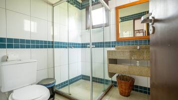 A bathroom with a glass shower enclosure, a toilet, a sink with a granite countertop, and a mirror above the sink.