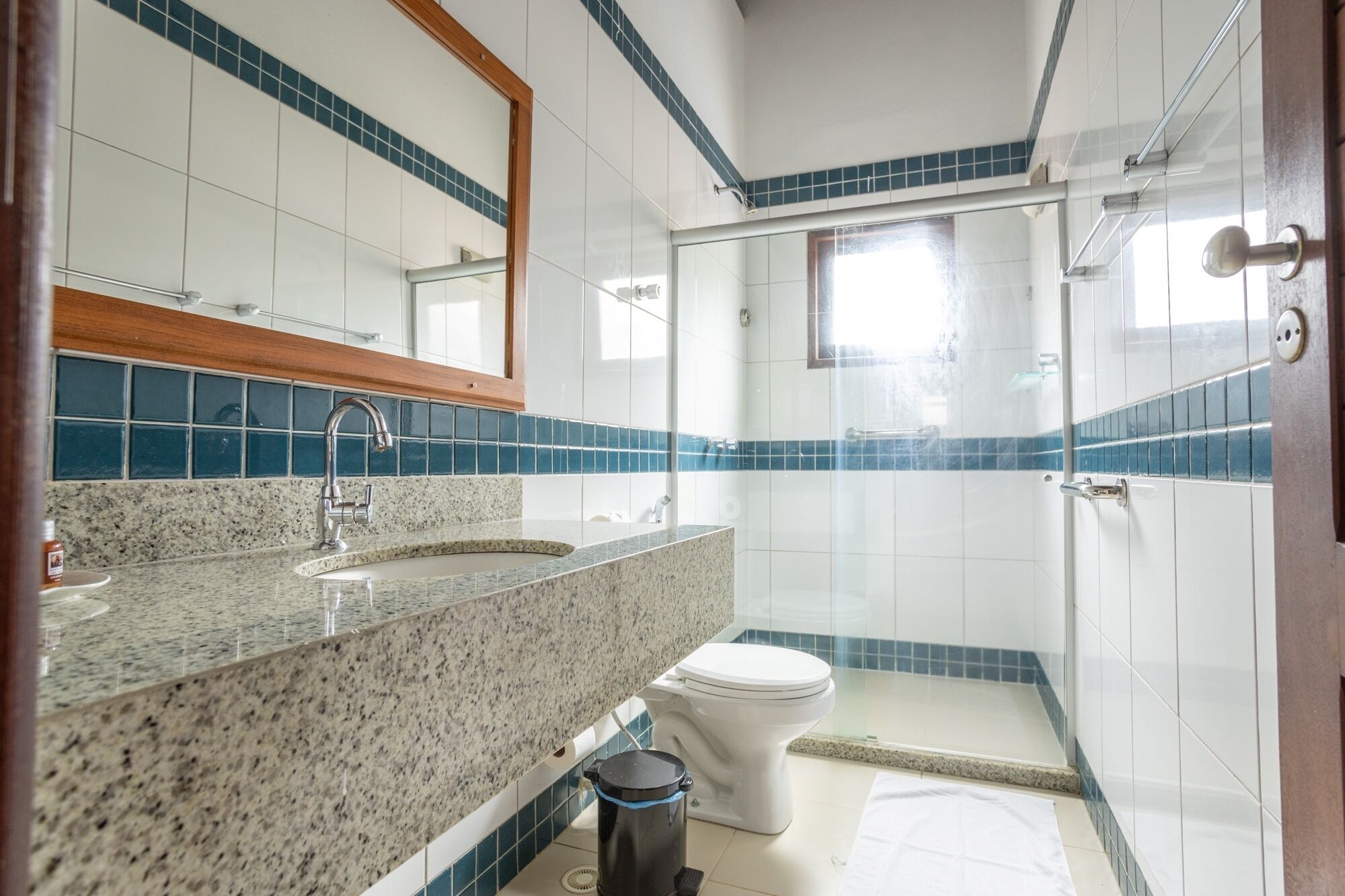 Un baño con lavamanos de encimera de granito, inodoro blanco y cabina de ducha con paredes de vidrio.
