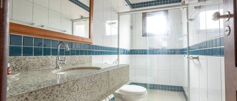Un baño con lavamanos de encimera de granito, inodoro blanco y cabina de ducha con paredes de vidrio.
