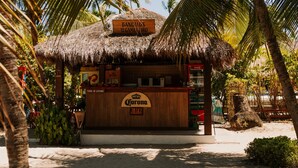 Eine Strandbar mit einem Reetdach, einem Corona-Schild und einem Schild mit der Aufschrift 'BANGALOS'.