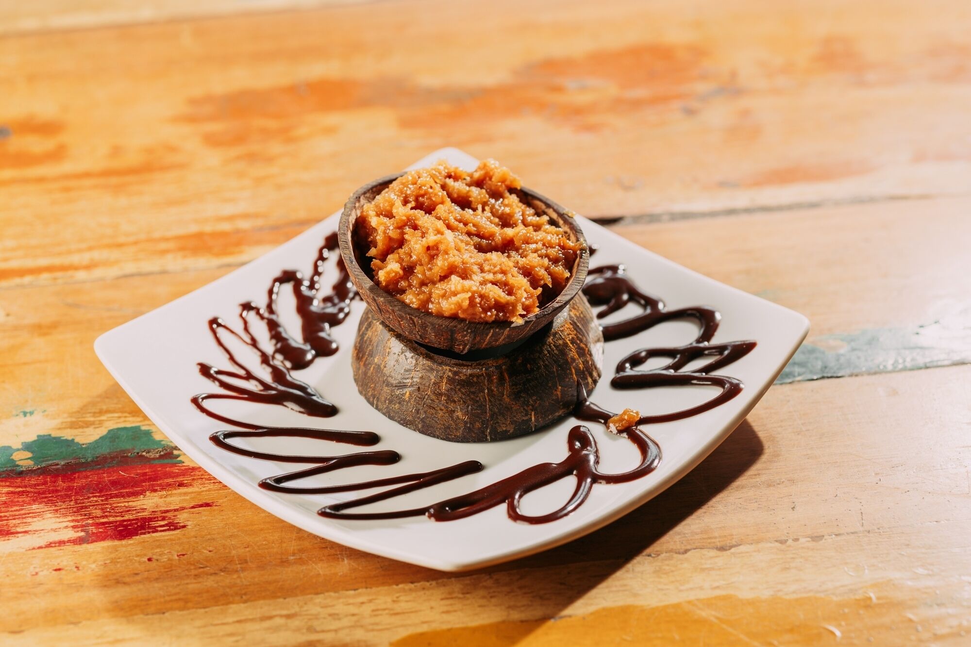 A dessert on a square plate with chocolate drizzle.