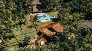 Ein Luftbild eines tropischen Resorts mit Swimmingpool, Hütten mit Strohdächern und üppiger Vegetation.