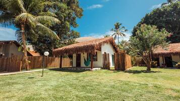 Una casa con techo de paja y un patio cubierto de hierba, rodeada de palmeras y otra vegetación.