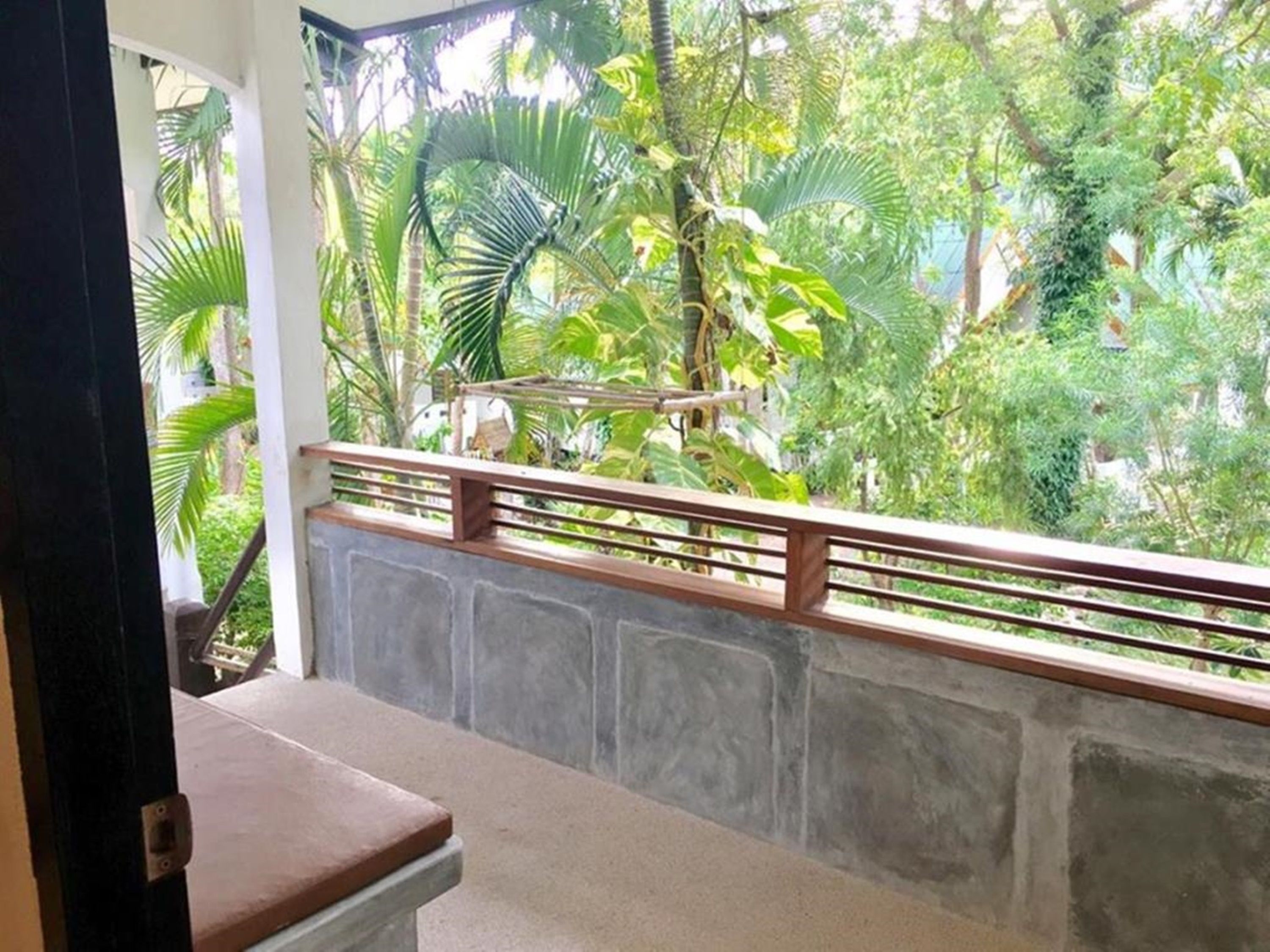 A balcony with a stone wall and a wooden railing overlooking a lush garden with various trees and plants.