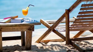 A wooden beach chair and a table with a drink and a book on a sandy beach with a clear blue sky in the background. - Fisherman Koh Tao (Koh Tao)