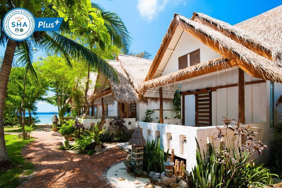 Ein Resort im Bungalowstil mit Reetdächern, Palmen und Meerblick.