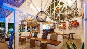 A cozy lounge area with wooden benches, hanging netted lights, and a bar in the background. - Fisherman Koh Tao (Koh Tao)