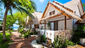 A traditional thatched-roof bungalow with a paved pathway leading to the entrance, surrounded by lush tropical vegetation and a view of the ocean. - Fisherman Koh Tao (Koh Tao)