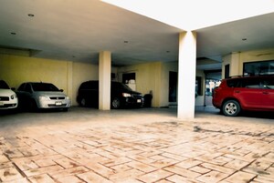 Un área de estacionamiento techada con tres coches aparcados en fila, suelo de baldosas y techo bajo con iluminación empotrada.