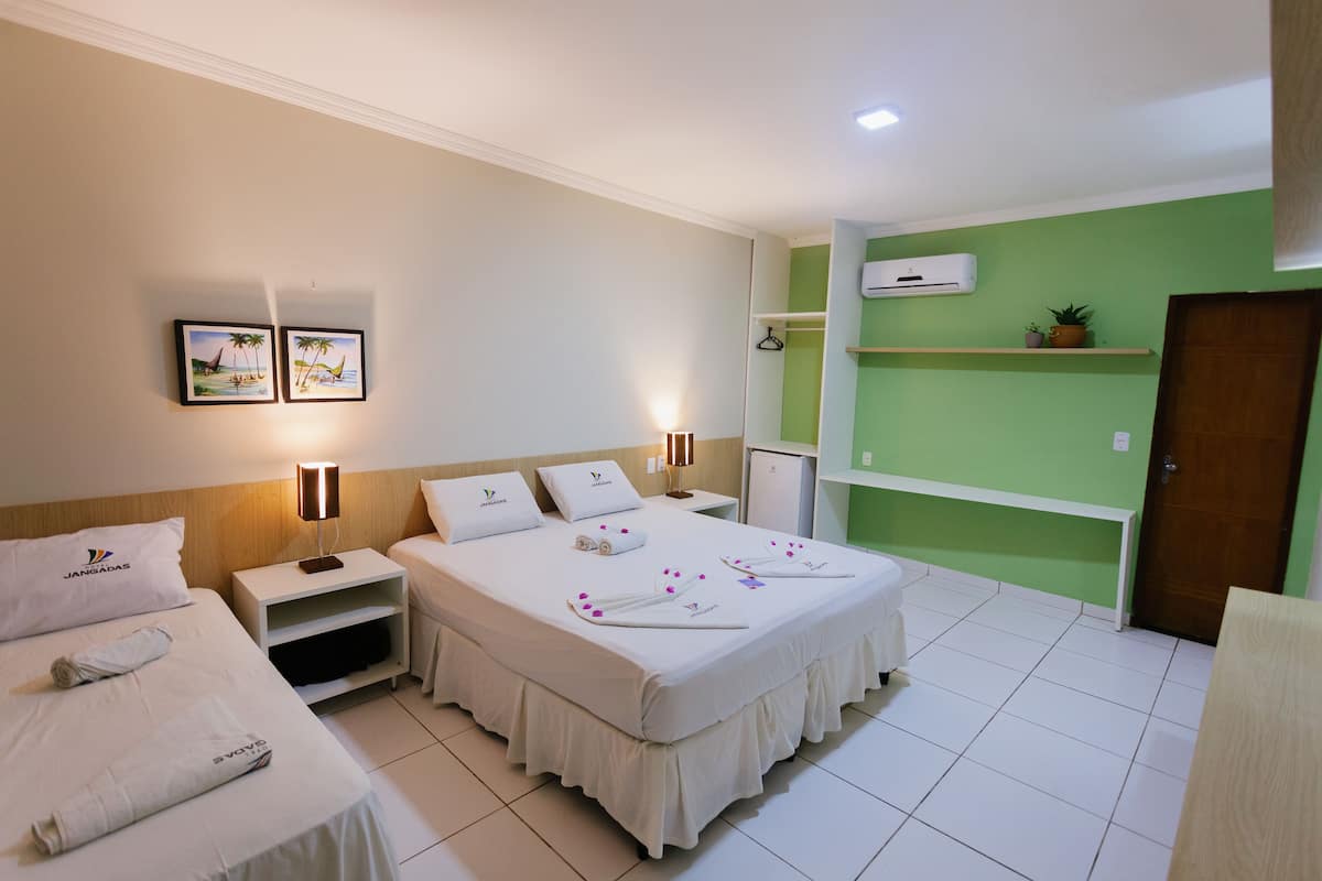 A hotel room with two beds, a bedside table with a lamp, a small desk, a green wall, and a door.