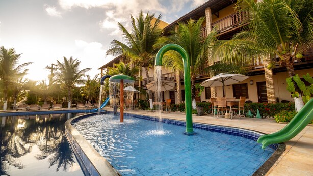 A swimming pool with a slide, palm trees, and a building with a balcony.