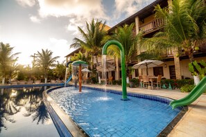 Piscina com escorregador, palmeiras e um edifício com varanda.