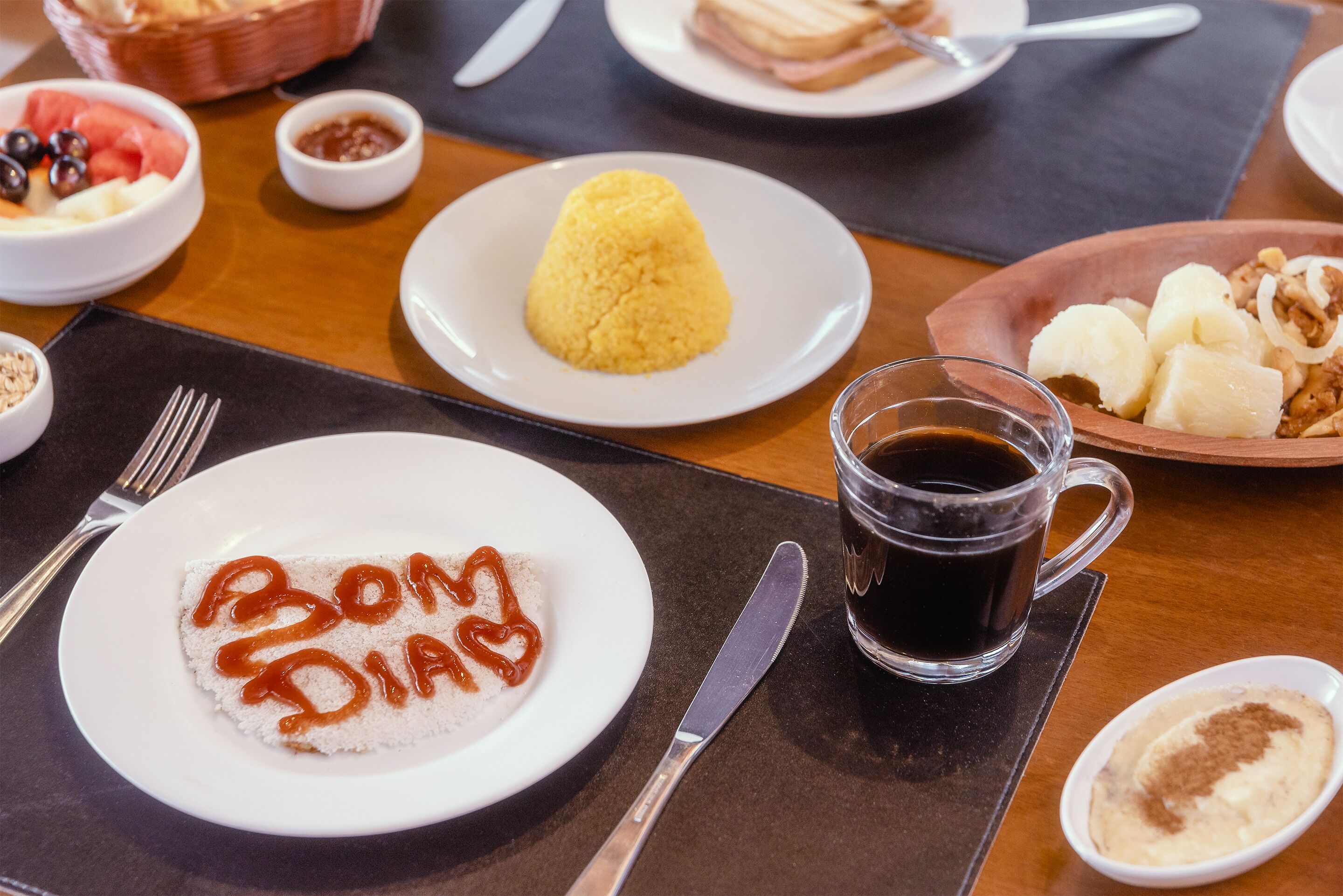 Una mesa de comedor con diversos platos, incluyendo arroz, pan y un plato con la inscripción 'Bom Dia'.