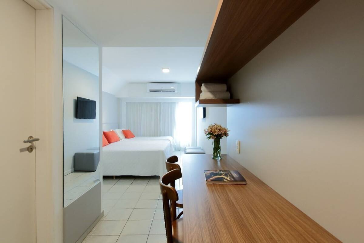 A modern hotel room with a bed, a desk, and a chair. There is a television mounted on the wall and a window with curtains.