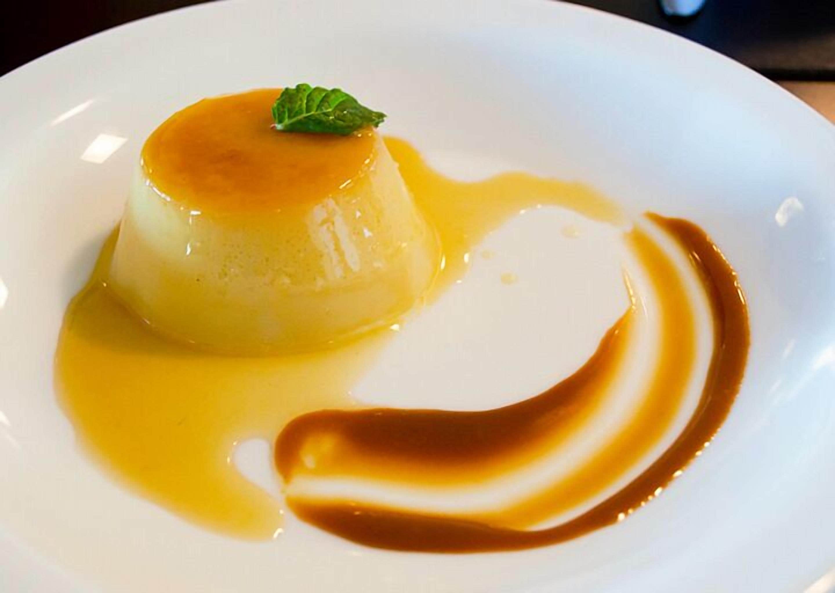 Un postre en un plato blanco con salsa de caramelo y una hoja de menta como adorno.