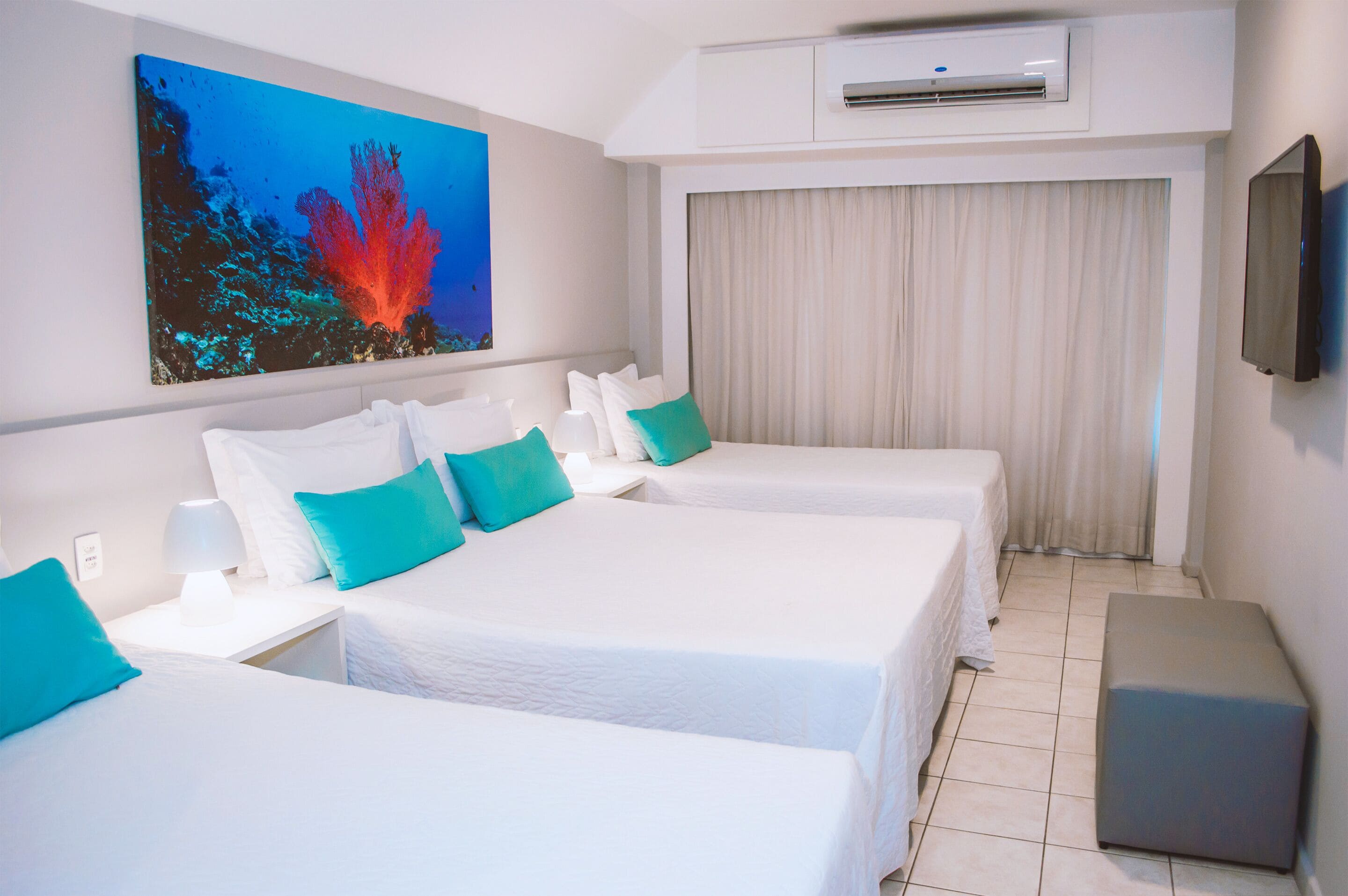 A hotel room with two beds, a painting of a coral reef, an air conditioning unit, and a television on the wall.