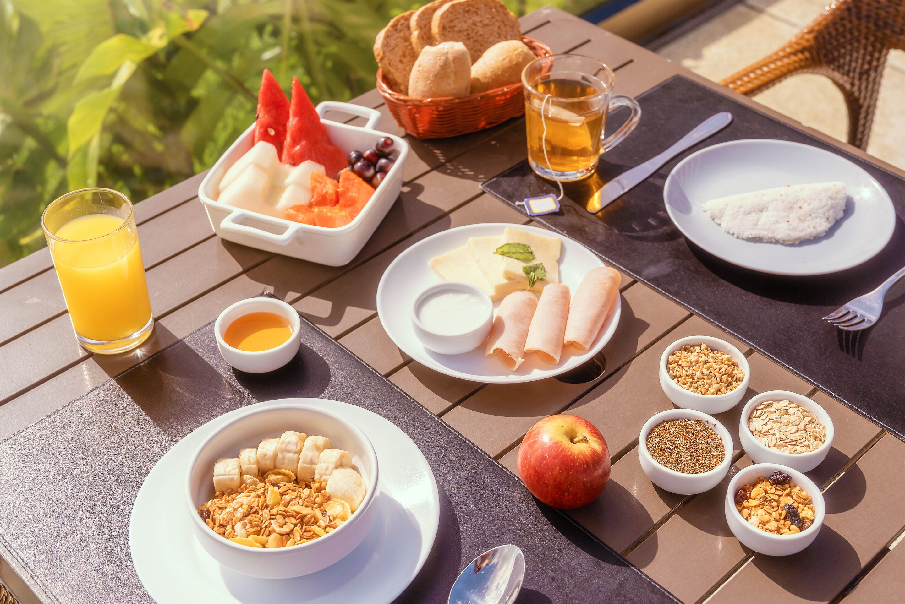 Mesa posta com itens de café da manhã, incluindo frutas, pão e diversas geleias.
