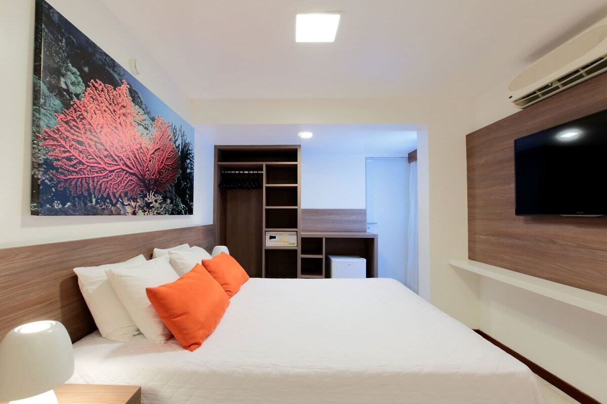 Ein Hotelzimmer mit einem Bett, einem Fernseher, einem Gemälde, einem Kleiderschrank und einem Schreibtisch.