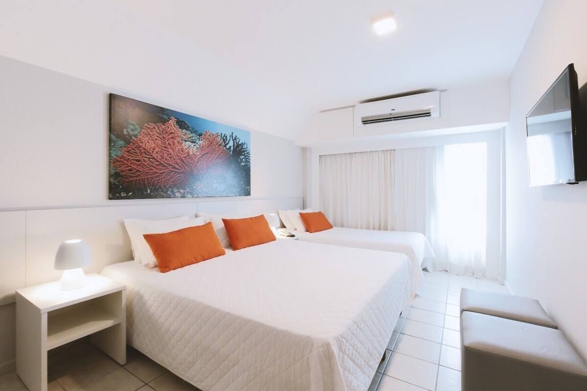 A hotel room with two beds, a painting on the wall, an air conditioning unit, a TV, and a window with curtains.