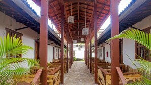 A covered walkway with wooden benches and stone flooring, flanked by walls and potted plants. - Jeri Village Hotel (Jijoca de Jericoacoara)