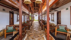 A corridor with wooden benches and stone flooring, leading to a central area with a view of the outdoors. - Jeri Village Hotel (Jijoca de Jericoacoara)