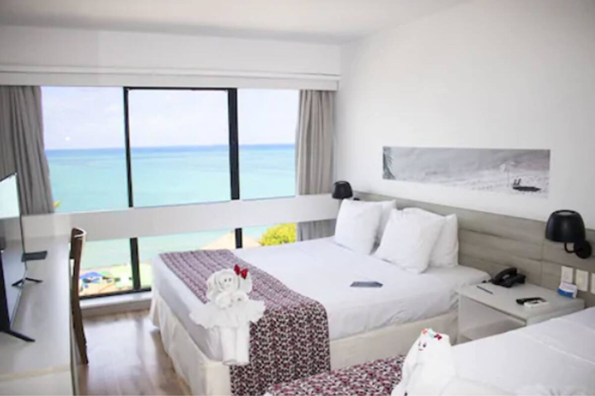 Une chambre d’hôtel avec un grand lit, un bureau, une chaise et une vue sur l’océan.