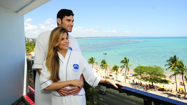 A couple on a balcony overlooking a beach with palm trees and a clear sky. - Maceió Mar Hotel (Maceió)