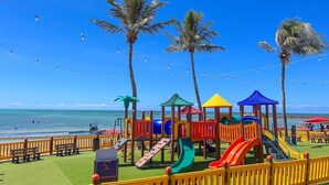 A beach playground with slides and play structures, palm trees, and a clear blue sky. - Maceió Mar Hotel (Maceió)