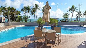 A pool area with a table and chairs, surrounded by palm trees and a view of the ocean. - Maceió Mar Hotel (Maceió)
