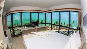 A hotel room with a large bed, a TV, and a view of the beach and ocean through large windows. - Maceió Mar Hotel (Maceió)