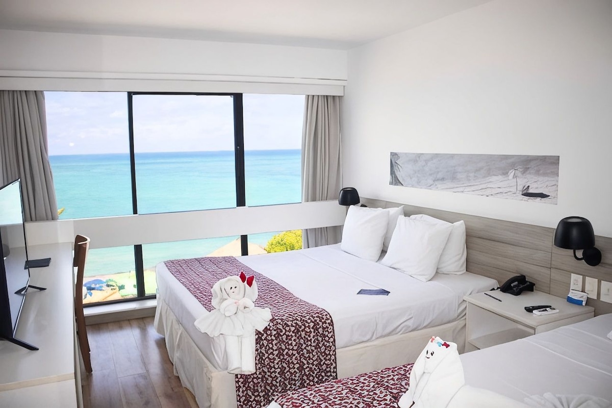 A hotel room with a large window, a bed, a desk, and a chair.