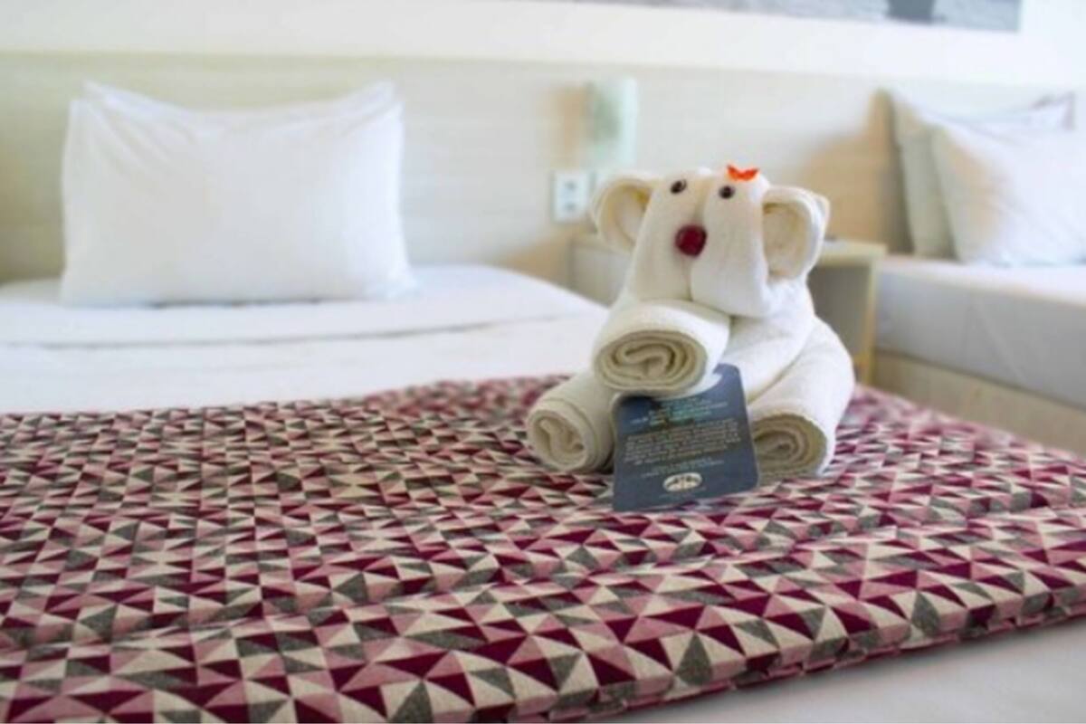 Un lit bien fait, avec une couverture à motifs, une serviette enroulée et un petit jouet en peluche ressemblant à un ours.