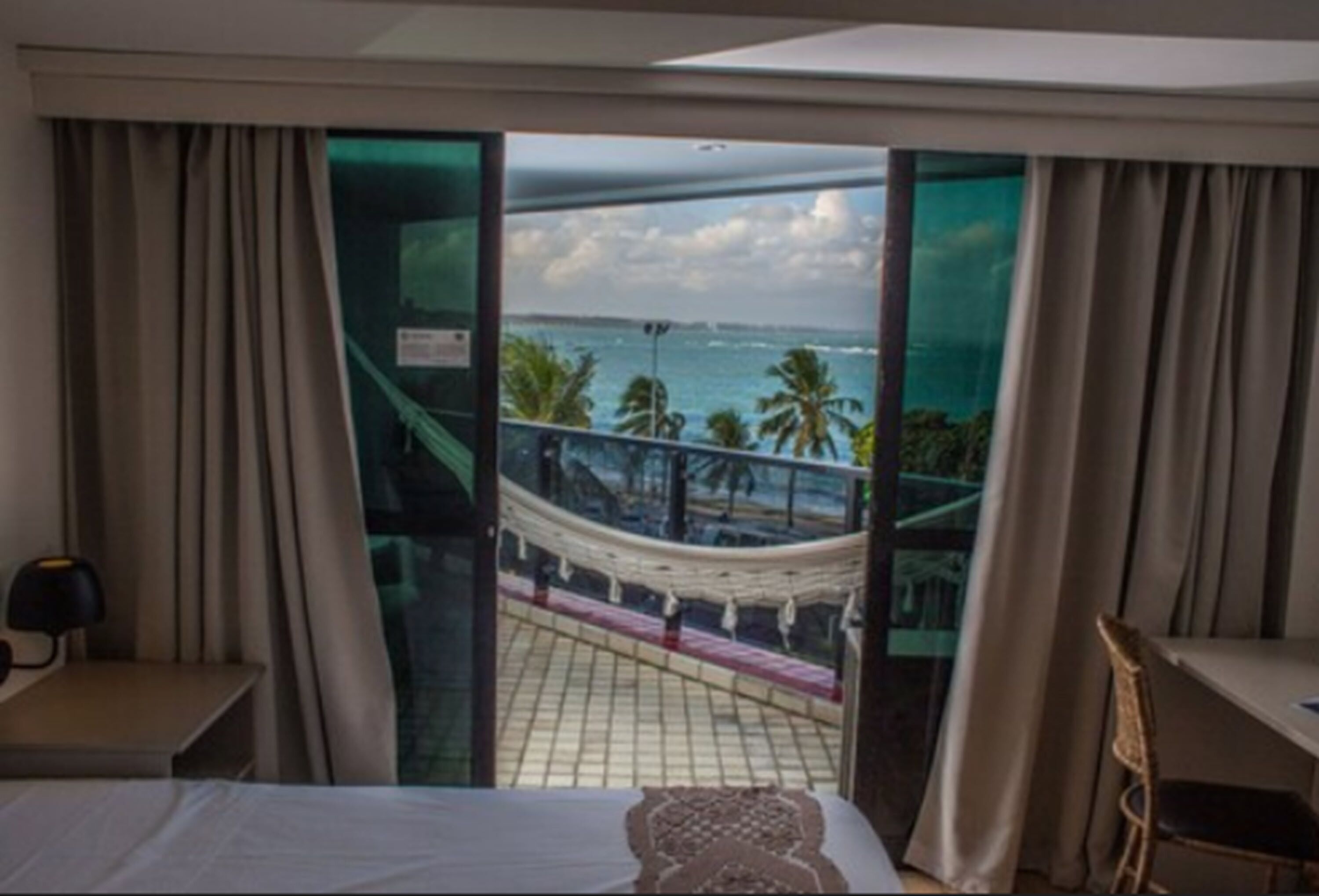 A hotel room with a bed, a nightstand, and a view of the sea through a glass door.