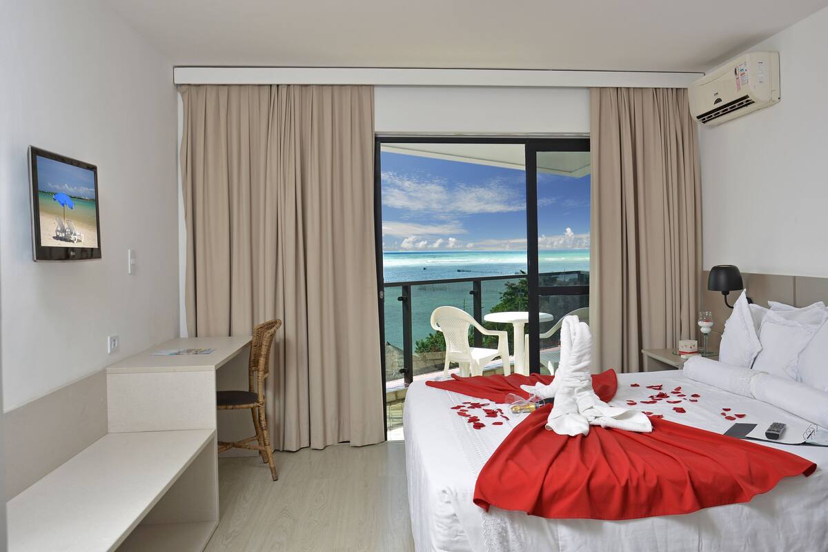 Une chambre d’hôtel équipée d’un lit, d’un bureau, d’une chaise, d’un balcon avec vue sur la mer et d’un appareil de climatisation.