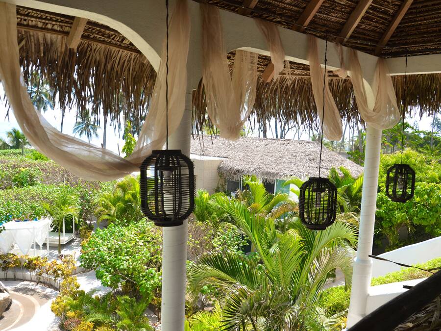 Un espacio al aire libre cubierto con techo de paja, faroles colgantes y abundante vegetación.