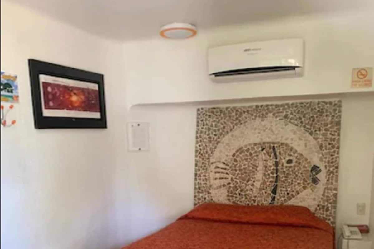 Ein Zimmer mit einem Bett, einer Wand-Klimaanlage, einem gerahmten Bild und einem Mosaikwerk.