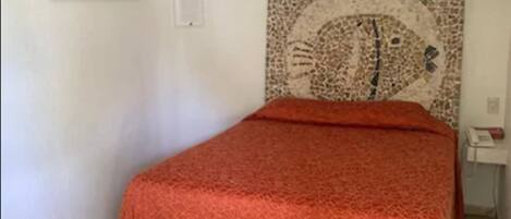 A room with a bed, a wall-mounted air conditioner, a framed picture, and a mosaic artwork.