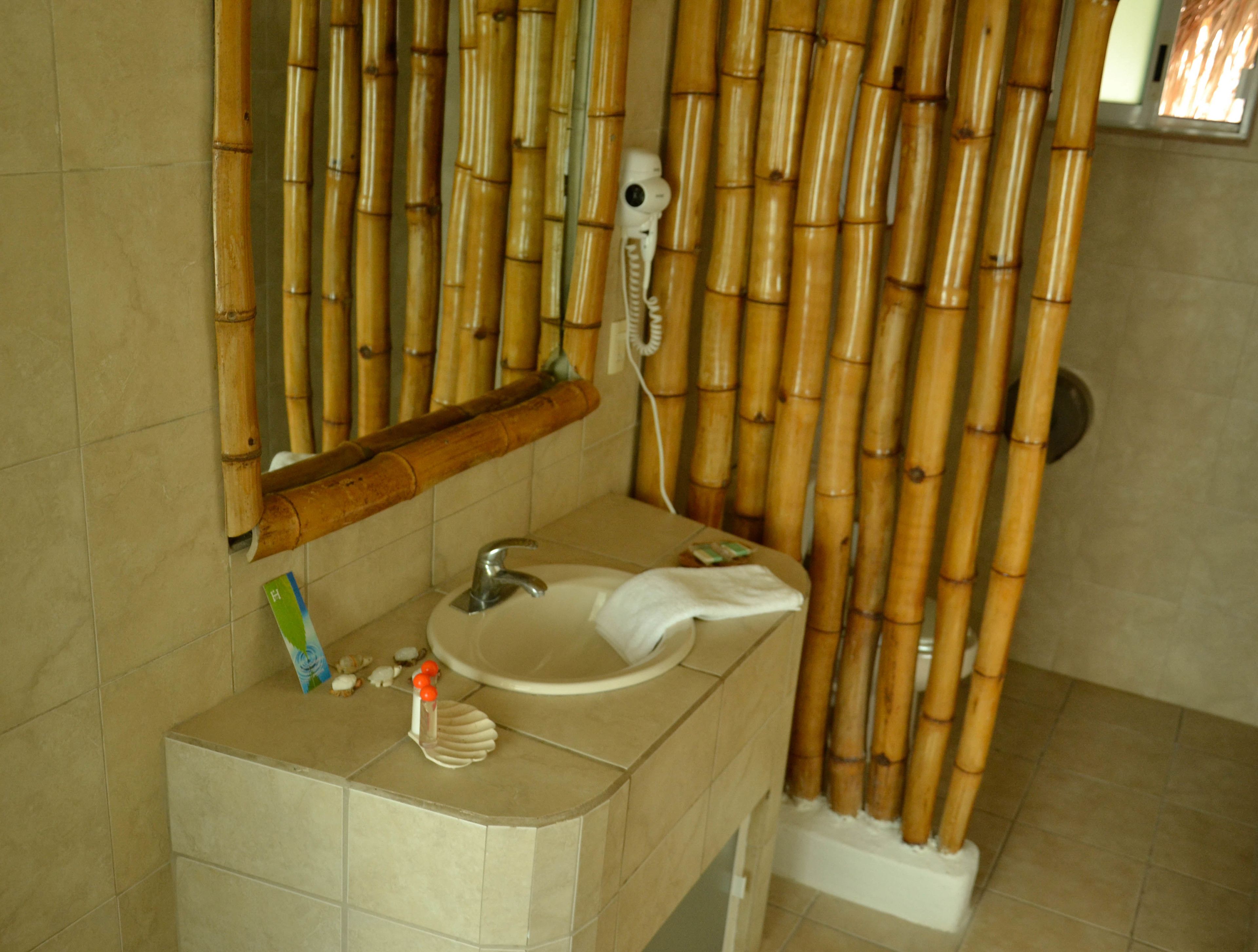 A bathroom with a bamboo shower curtain, a sink with a mirror above it, and a towel hanging on the wall.