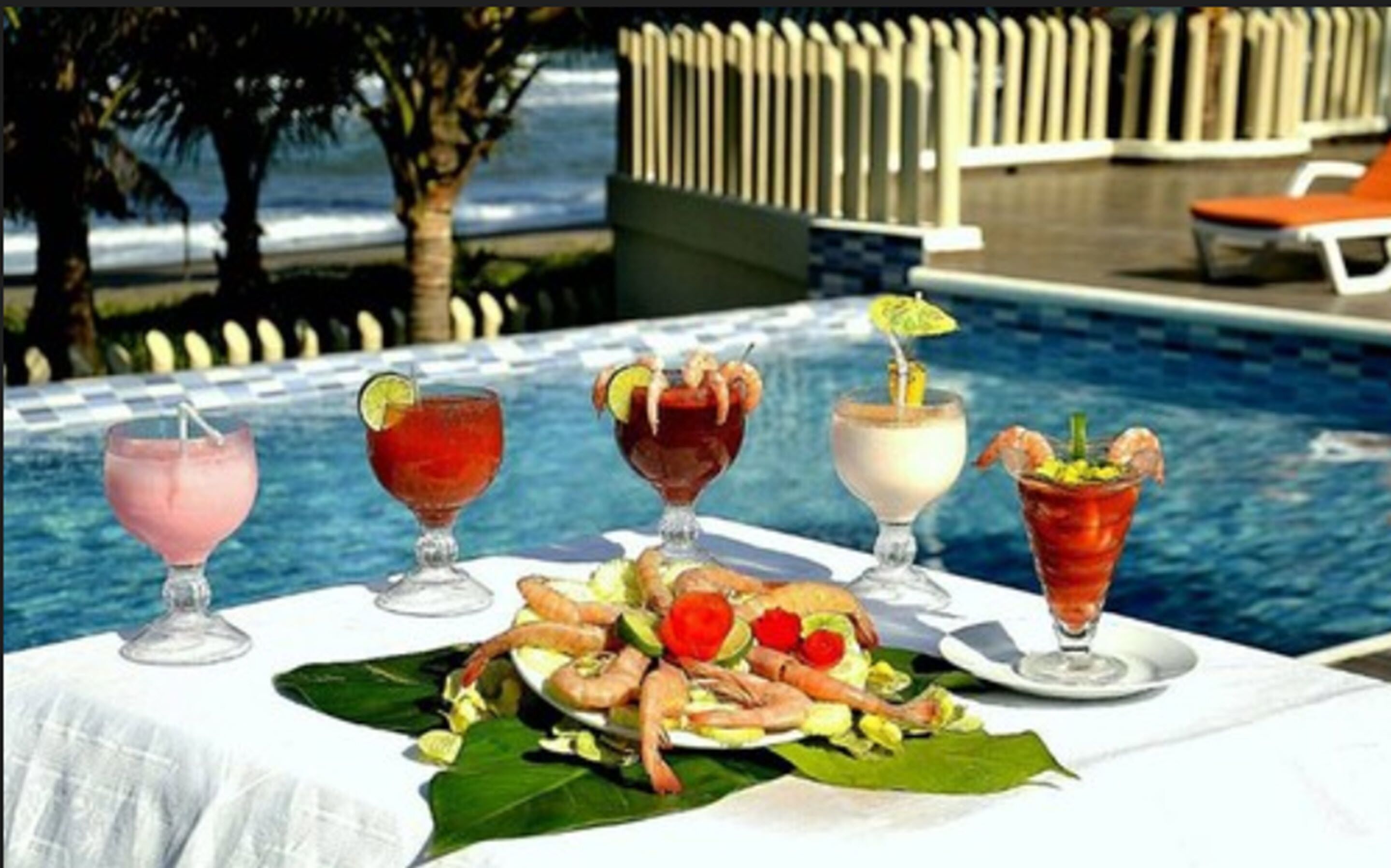 Une table placée au bord de la piscine, avec des boissons et des amuse-gueules aux crevettes.