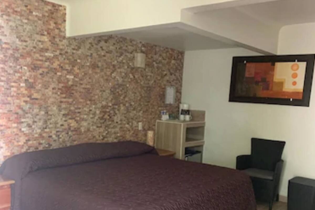 Ein Schlafzimmer mit einem großen Bett, einem Schreibtisch, einem Stuhl und einem an der Wand hängenden Kunstwerk.